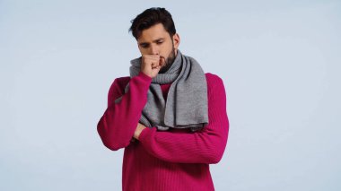 Hırkalı ve eşarplı hasta adam mavi üzerinde yalnız öksürüyor. 
