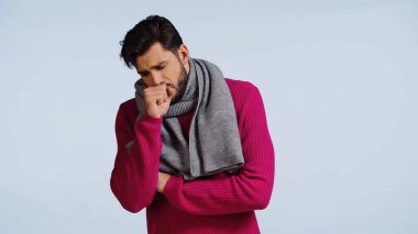 Pembe kazaklı ve atkılı hasta adam mavi üzerine öksürüyor. 