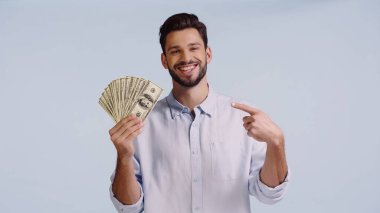 Mavi üzerine izole edilmiş dolarları gösterirken kameraya bakan gömlekli neşeli bir adam. 