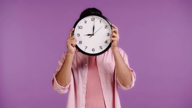 young man obscuring face with clock isolated on purple clipart
