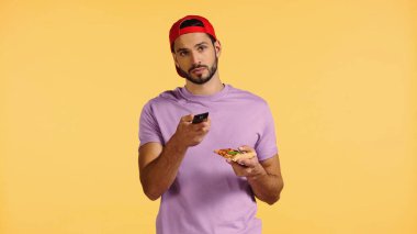 Sakallı adam elinde pizzayla televizyon seyrediyor. 