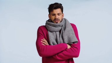 Pembe kazaklı ve atkılı hasta adam mavi kolları çapraz duruyor. 