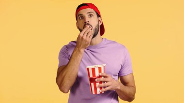 Adam film izliyor ve sarı üzerine izole edilmiş patlamış mısır yiyor.