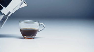 Kahve makinesi, cam fincanın yanında, beyaz ve gri üzerine kahve. 