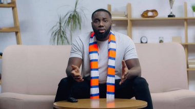 Üzgün Afro-Amerikan spor fanatiği ev televizyonunda şampiyonluk maçı izlerken elleri ile işaret ediyor.