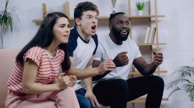 Mutlu ırklar arası dostların yanında çığlık atan heyecanlı adam televizyonda spor müsabakaları izliyor.