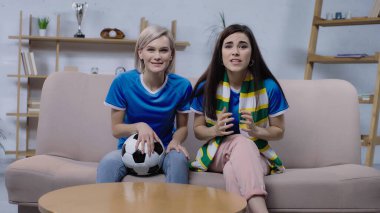 Kanepede futbol topuyla oturan heyecanlı kadınlar,