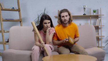 Softbol ekipmanlı üzgün arkadaşlar kanepede ve evde oturup TV 'de maç izliyorlar.