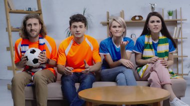 Duygusal arkadaşlar, evdeki kanepede futbol şampiyonasını izlerken elleri ile işaret ediyorlar.