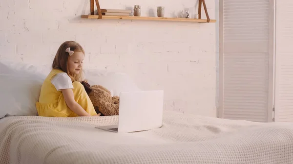 Ребенок Смотрит Ноутбук Возле Мягкой Игрушки Кровати Дома — стоковое фото