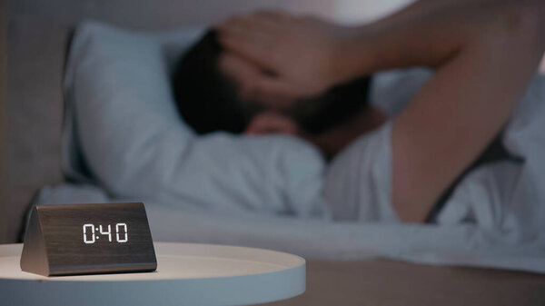 Clock on bedside table near blurred man on bed at night 