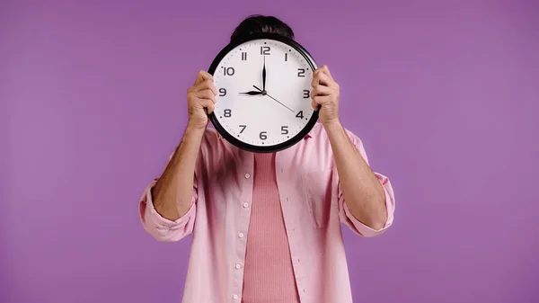 ピンクのシャツを着た若い男が顔を隠して紫色に隔離された時計で — ストック写真