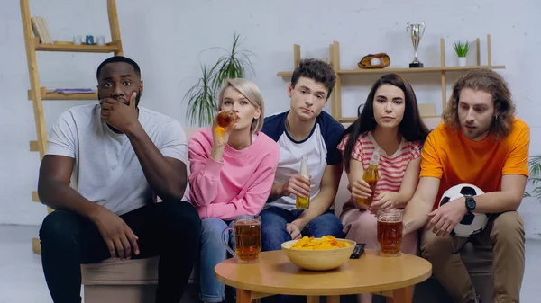 Genç bir kadın, çok ırklı arkadaşlarıyla futbol şampiyonası izlerken bira içiyor.