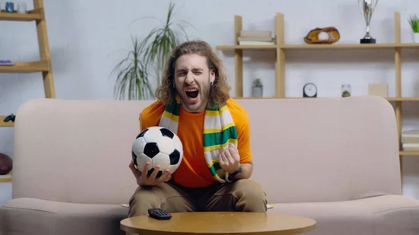 Excited Man Holding Soccer Ball Showing Triumph Gesture While Watching — Stock Photo, Image