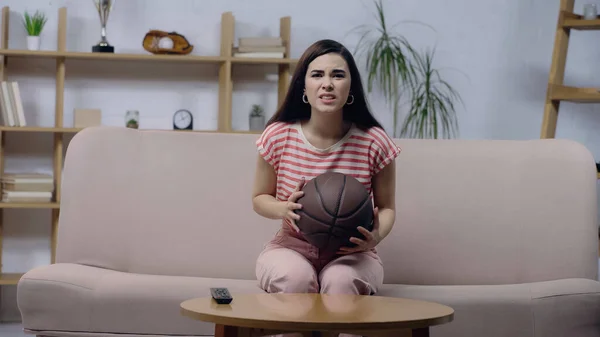 ホームテレビでバスケットボールの試合を見ながらボールを持っているスポーツファンの女性を心配 — ストック写真