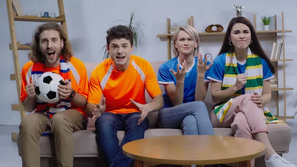 emotional friends gesturing while sitting on couch and watching football championship