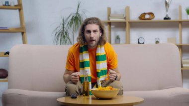 Evde TV 'de yarışma izlerken, sporseverler şans için yumruklarını sıkarlar.