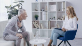muž středního věku ve sportovním oblečení sedí na pohovce a mluví s veselým psychologem v ordinaci