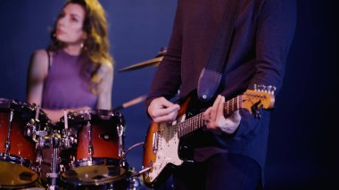 KYIV, UKRAINE - DECEMBER 30, 2021: rock guitarist playing near blurred and pretty drummer on stage