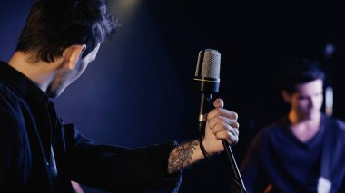 tattooed singer near microphone and blurred musician on stage