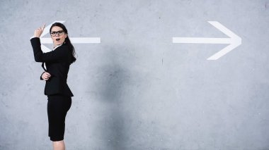 surprised businesswoman in glasses having idea near arrows on grey