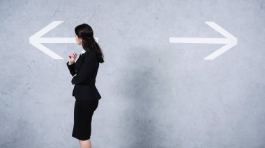 thoughtful businesswoman in suit looking at arrows on grey