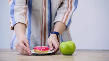 cropped view of woman holding plate with doughnut near apple isolated on grey