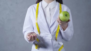 cropped view of nutritionist comparing apple and vitamins on grey clipart