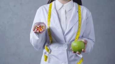 partial view of nutritionist comparing apple and vitamins on grey  clipart