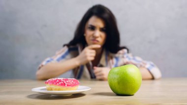 blurred woman choosing between apple and doughnut on grey