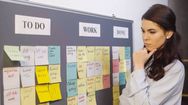 pensive businesswoman thinking near colorful sticky notes on board clipart