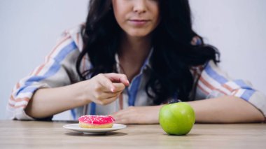 cropped view of woman pointing at apple near doughnut isolated on grey