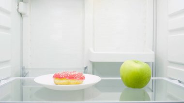 sweet glazed doughnut on plate near green apple in fridge