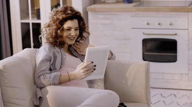 Evde dijital tablet kullanırken gülümseyen hamile kadın 