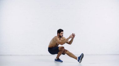 Şortlu ve spor ayakkabılı sakallı sporcu beyaz tuğla duvarın yanında çalışıyor.