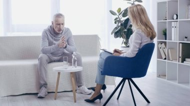 mature sportsman and blonde psychologist having conversation in consulting room clipart