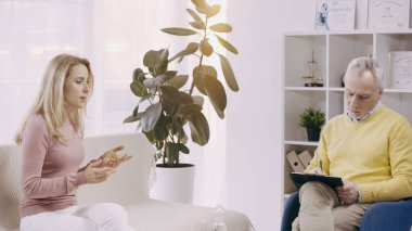 Olgun psikolog, duygusal sarışın kadının yanında panoya yazı yazıyor. 