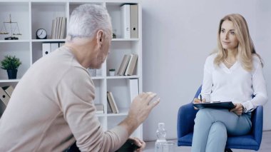 Sarışın psikolog muayene sırasında orta yaşlı bir hastaya bakıyor. 