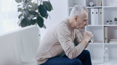 side view of upset middle aged man talking in consulting room during psychotherapy  clipart