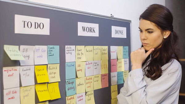 pensive businesswoman thinking near colorful sticky notes on board