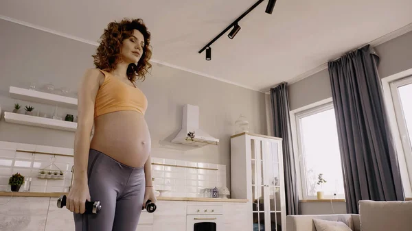 低角度ビューの妊娠中の女性保持ダンベルに家 — ストック写真