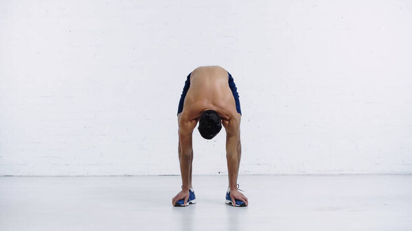 shirtless sportsman doing forward leaning near white brick wall