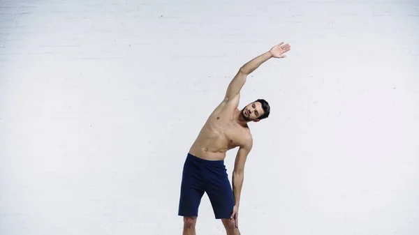 Young Sportsman Stretching White Brick Wall — Stock Photo, Image