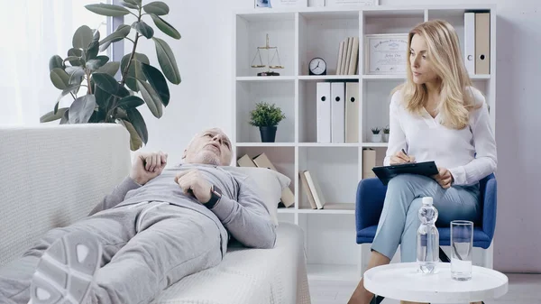 Middle Aged Man Sportswear Lying Sofa Talking Blonde Psychotherapist Clipboard — Fotografia de Stock