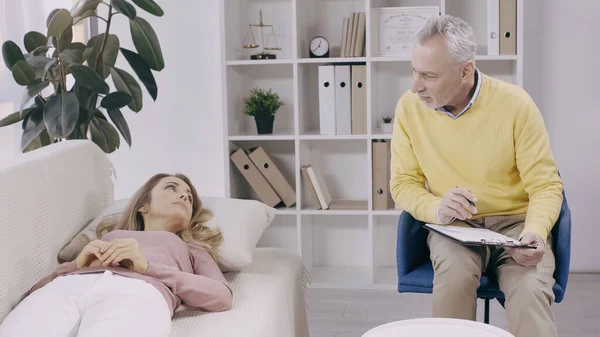 Blonde Woman Lying Couch Looking Middle Aged Psychotherapist Clipboard Consultation — 图库照片