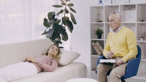 Blonde Frau Liegt Auf Couch Neben Nachdenklichem Psychotherapeuten Mittleren Alters — Stockfoto