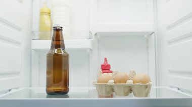 Buzdolabında bir şişe bira, süt, yumurta ve sos.