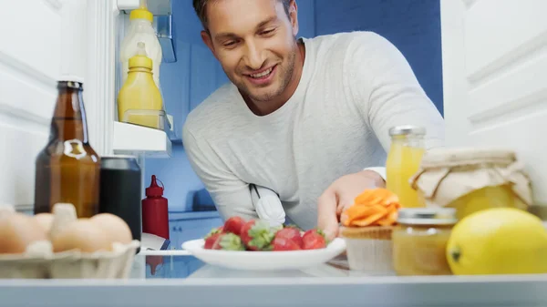 Joyful Man Taking Ripe Strawberries Fridge Beverages Sauces Eggs Jars — Stock Photo, Image