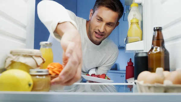 Joyful Man Taking Delicious Cupcake Strawberries Fridge Drinks Eggs Containers — Stock Photo, Image