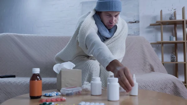 Ill Man Warm Blanket Hat Reaching Nasal Spray While Sitting — стоковое фото